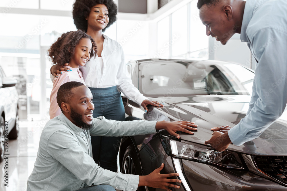 Car sales business. Young black family with cute child selecting vehicle, looking at luxury automobile at showroom. Seller talking to Afro clients, showing them new auto at dealership shop Car sales business. Young black family with cute child selecting vehicle, looking at luxury automobile at showroom. Seller talking to Afro clients, showing them new auto at dealership shop