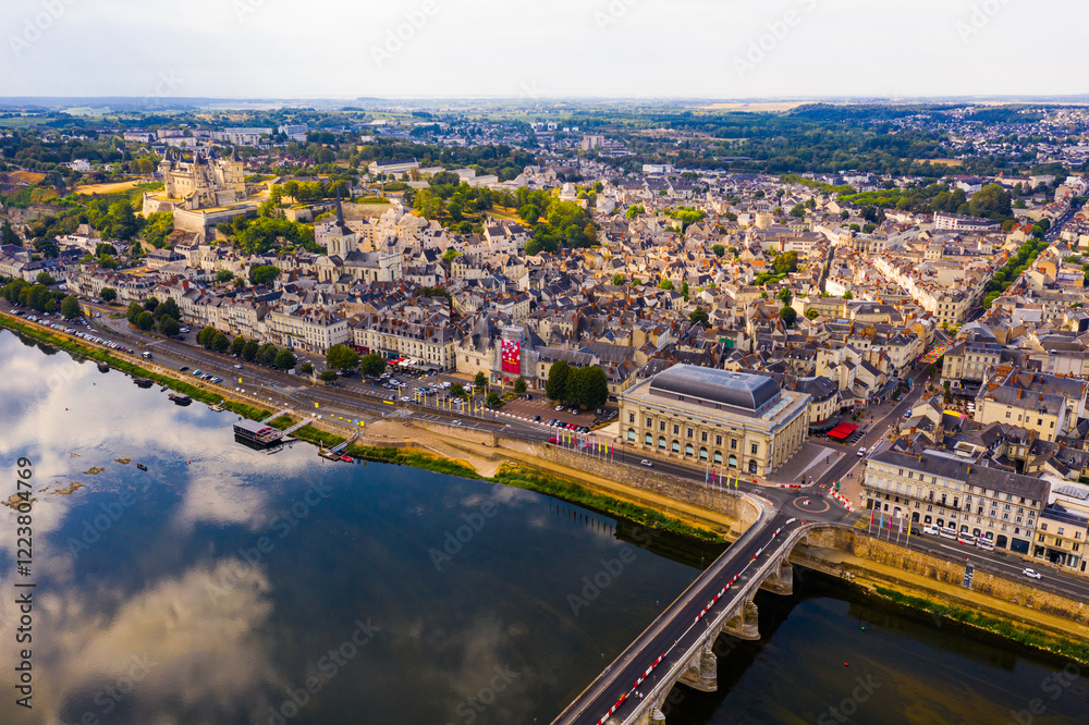 Fototapeta premium Drone view of summer cityscape of Saumur overlooking theatre Le Dome on bank of Loire River with medieval fortified Chateau on background, France