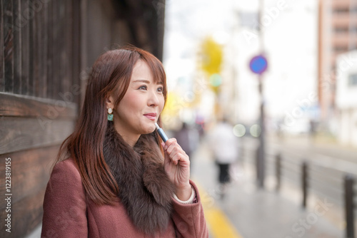 Next to the historical buildings in Japan. A Japanese woman with long hair in her thirties is looking at the city by smoking electronic cigarettes.