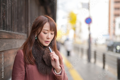 Next to the historical buildings in Japan. A Japanese woman with long hair in her thirties is looking at the city by smoking electronic cigarettes.