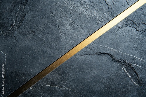 A sleek golden metal strip diagonally positioned on a textured dark stone surface, creating contrast