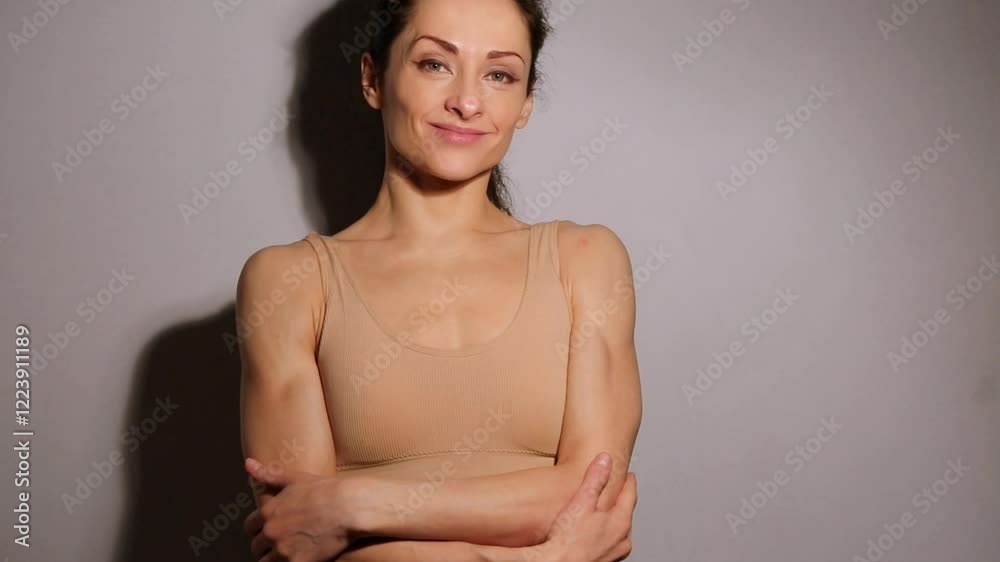 Smiling cute beautiful woman looking and touching her healthy arms skin on empty space background in studio low key light. Closeup facial emotional video. Sporty natural makeup female in sport bra