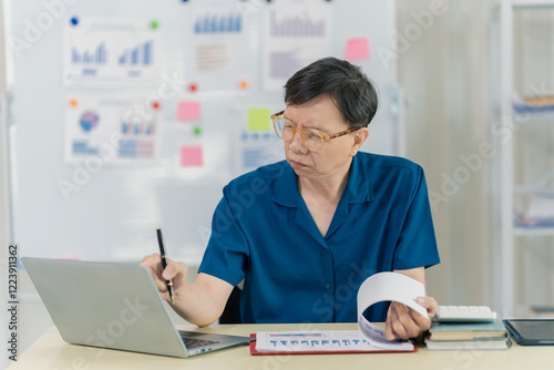 Senior Asian businessman working online using modern laptop computer Typing on his laptop while working from home, well organized. By emphasizing work using technology. photo