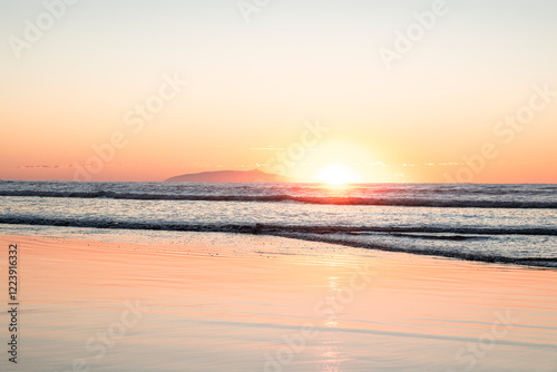 Sunrise scene at the beach over Pacific ocean  - sun coming from behind the waves lighting up the clear sky with bright yellow and orange colors. El Cuco Beach, El Salvador.