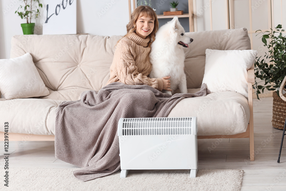 Young woman with plaid and her Samoyed dog on sofa warming near radiator at home Young woman with plaid and her Samoyed dog on sofa warming near radiator at home