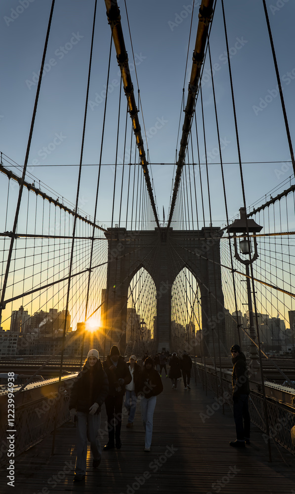 Fototapeta premium brooklyn bridge at sunrise (new york city landmark over east river to manhattan) travel tourism famous destination in usa america united states (suspension cables lamp light streetlight) people cross
