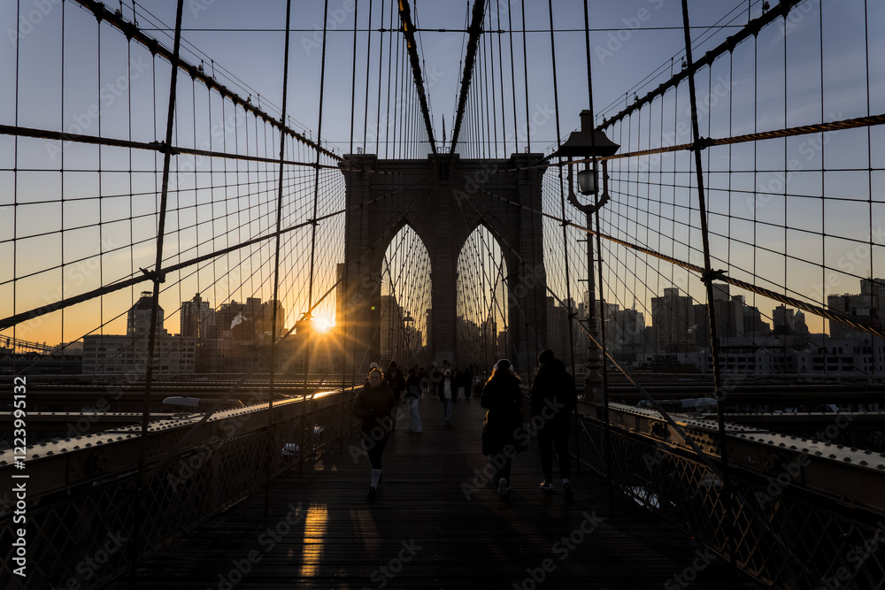 Fototapeta premium brooklyn bridge at sunrise (new york city landmark over east river to manhattan) travel tourism famous destination in usa america united states (suspension cables lamp light streetlight) people cross