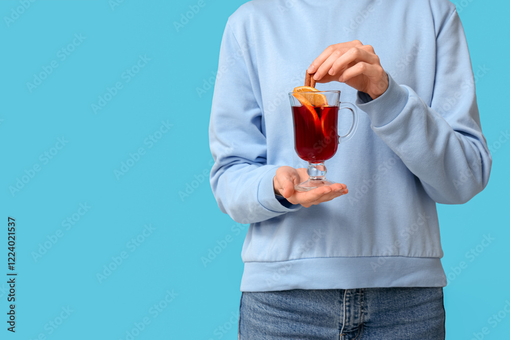 Young woman holding glass cup of hot mulled wine on blue background