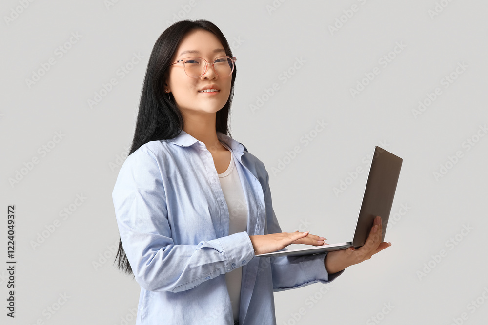 Beautiful young Asian woman with modern laptop on grey background