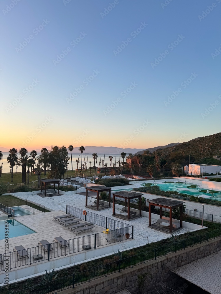 Fototapeta premium Beautiful sunset view over calm waters and resort pools near coastal palm trees