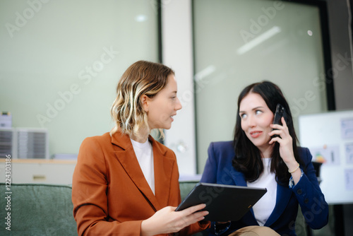 Two women collaborating on a project on sofa at home, brainstorming with a laptop and notebook
