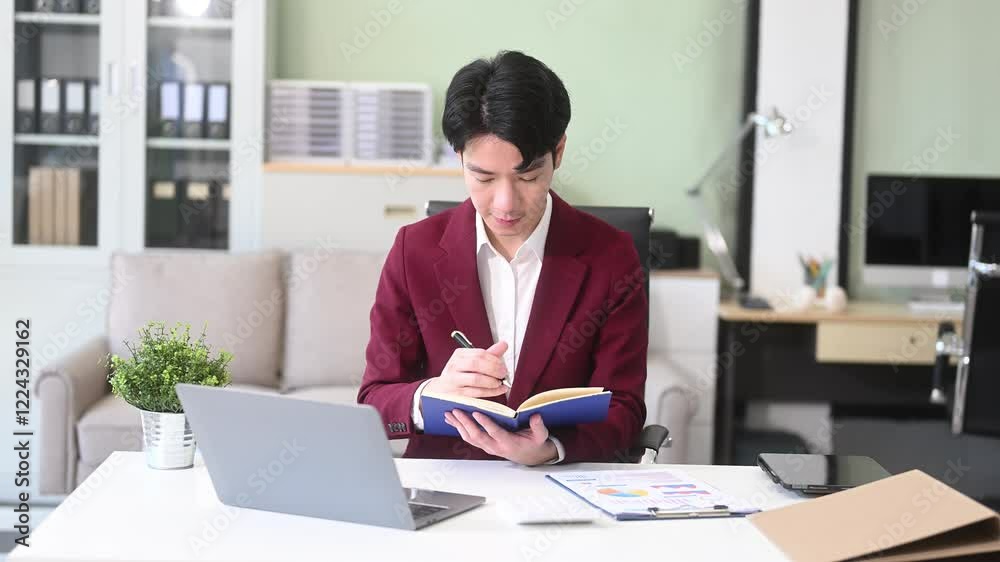 Asian entrepreneur focused on work, analyzing documents with a laptop on sofa in a stylish office. Asian entrepreneur focused on work, analyzing documents with a laptop on sofa in a stylish office.