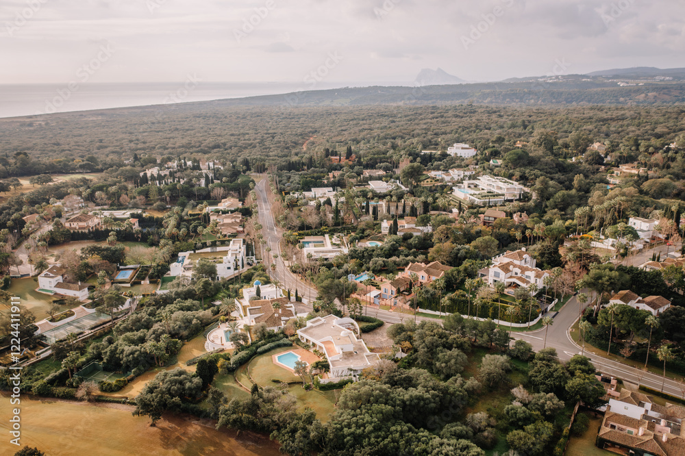 Fototapeta premium Aerial view of a residential area surrounded by lush greenery, with the coastline and the Rock of Gibraltar visible in the distance.