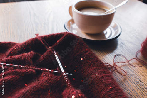 Obraz na płótnie Red knitted sweater with sequins and knitting needles with coffee cup on table. Sequin pattern in needlework with cappuccino. Knitting hobby. Knitted fashion concept. Sequins pattern in knitwear. w salonie