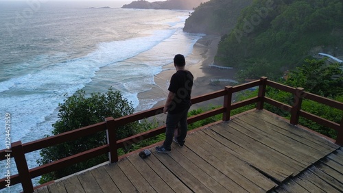  A man standing in the top of hill in coastline with hills, cliffs, trees, beach sand and waves from the sea and ocean at Lampon Beach, Kebumen, Central Java, Indonesia photo