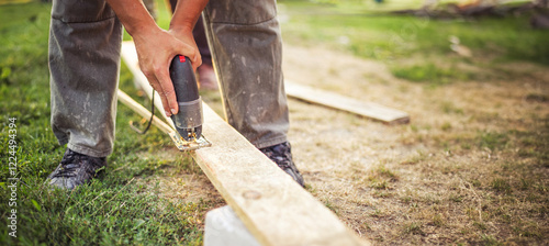 Obraz na płótnie Man uses an electric saw to cut a plank. Close-Up of a Carpenter's Hands Operating a Power Saw on Wood w salonie