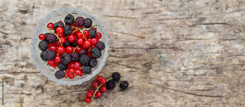 Summer fresh berries blackberry and red currant in a bowl on rustic wooden table. Flat lay, copy space.
