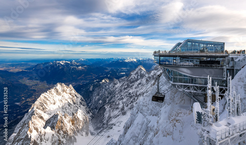 The Zugspitze near Garmisch-Partenkirchen (Bavaria) is the highest mountain in Germany. Panorama at the mountain station with cable car and view of the Alpine foothills on a sunny snowy December day.