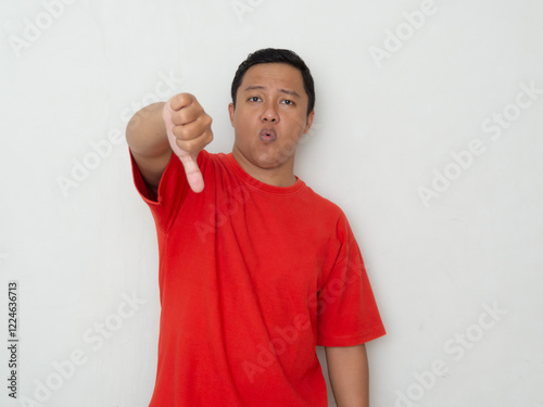 Young Asian man in red shirt giving a thumbs-down gesture with a displeased expression. concept of conveying disapproval, dissatisfaction, or negative feedback. photo