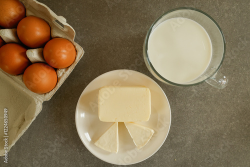 Butter, milk, eggs, and cheese on a gray countertop, photographed from a top view. photo