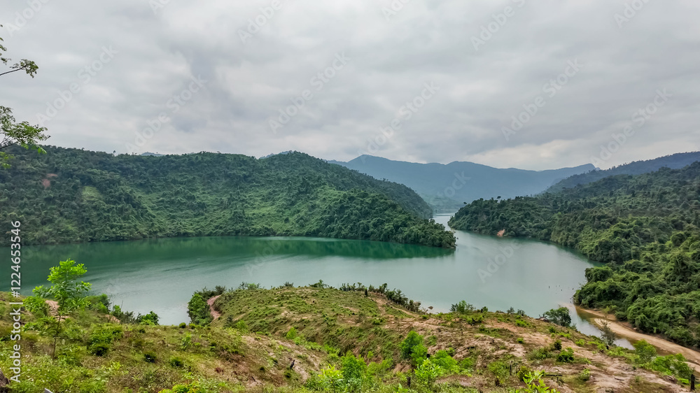 Serene view of a lush green hillside overlooking a tranquil lake under overcast skies, perfect for eco-tourism and nature exploration Serene view of a lush green hillside overlooking a tranquil lake under overcast skies, perfect for eco-tourism and nature exploration