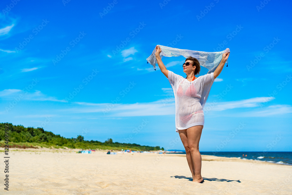 Beautiful mature woman holding scarf fluttering in wind standing on sandy beach. Front view Beautiful mature woman holding scarf fluttering in wind standing on sandy beach. Front view