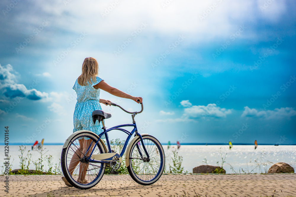 Summertime activity. Beautiful mature woman wearing summer dress standing with cruiser bike on bicycle path on seafront on sunny day. Back view Summertime activity. Beautiful mature woman wearing summer dress standing with cruiser bike on bicycle path on seafront on sunny day. Back view