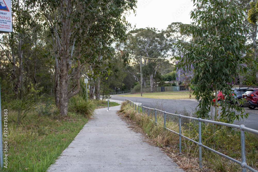 Scenic pathway lined with vibrant pink-red flowers and lush greenery, leading through an international peace park in Western Sydney, Australia. Parking area visible under a canopy of trees. Scenic pathway lined with vibrant pink-red flowers and lush greenery, leading through an international peace park in Western Sydney, Australia. Parking area visible under a canopy of trees.