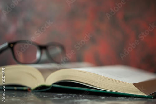 Open book lying on tabletop and glasses lying on book, red blurry wall in background. Space for text, design.