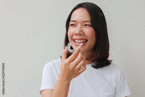 close up young asian beautiful woman smiling with hand holding dental aligner retainer (invisible) at dental clinic for beautiful teeth treatment course concept