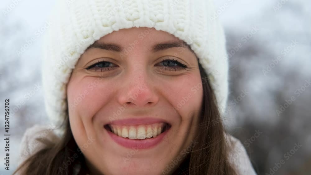 Portrait of woman in warm white knitted hat outdoors in winter. Young woman smiling and enjoying beautiful weather and first snow, laughing and looking at camera. Active winter recreation. Wide Portrait of woman in warm white knitted hat outdoors in winter. Young woman smiling and enjoying beautiful weather and first snow, laughing and looking at camera. Active winter recreation. Wide