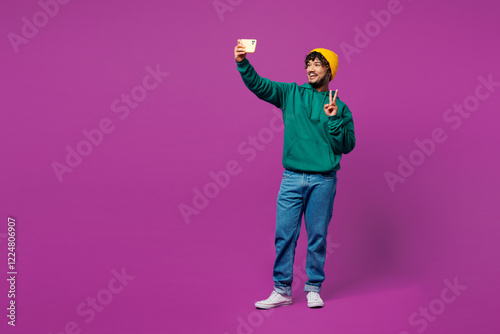 Photography Full body young happy Indian man he wear green hoody yellow hat casual clothes do selfie shot on mobile cell phone post photo on social network isolated on plain purple background