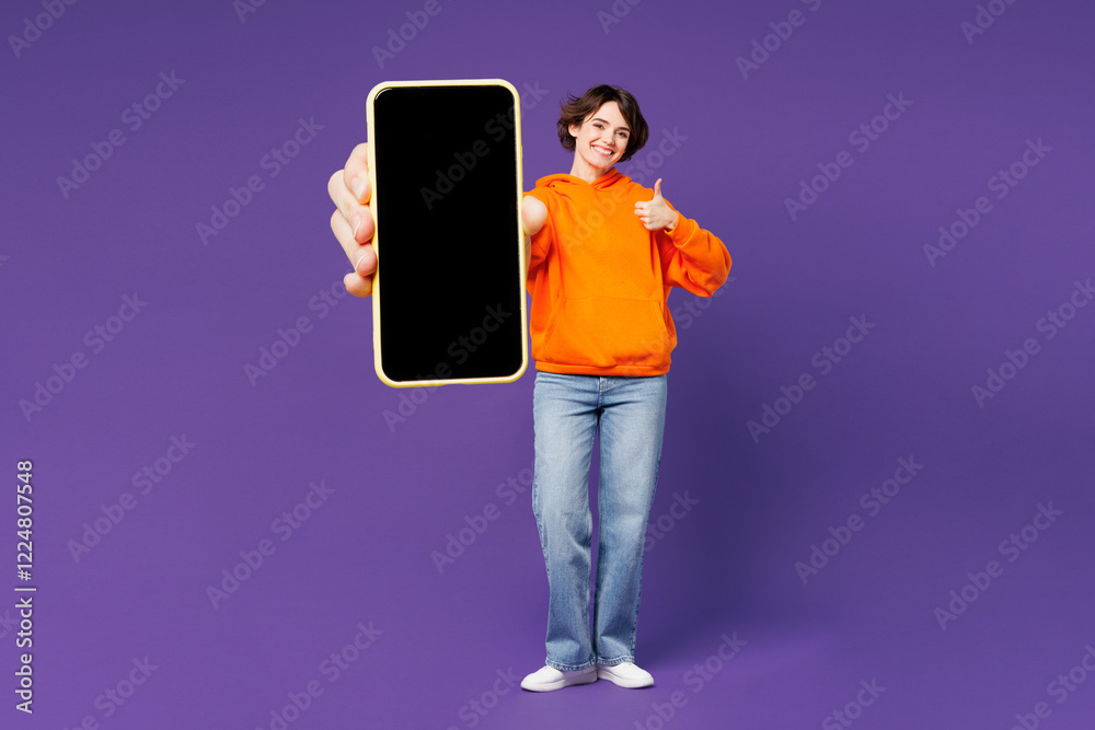 © ViDi Studio - Full body young smiling happy woman wear orange hoody casual clothes hold in hand use close up mobile cell phone show thumb up isolated on plain purple background studio portrait. Lifestyle concept. © ViDi Studio - Full body young smiling happy woman wear orange hoody casual clothes hold in hand use close up mobile cell phone show thumb up isolated on plain purple background studio portrait. Lifestyle concept.