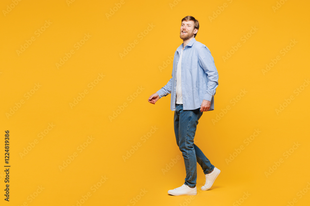 Fototapeta premium Full body side profile view young smiling cheerful fun happy man he wear blue shirt t-shirt casual clothes walking going isolated on plain yellow orange background studio portrait. Lifestyle concept.