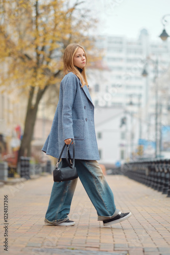 A fashionable young woman strolls a city street on a cloudy day in her trendy outfit
