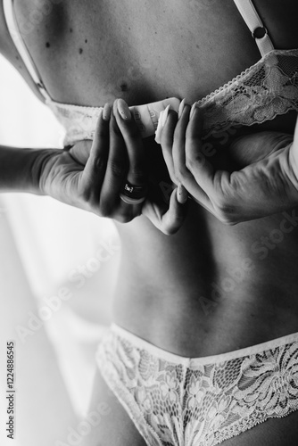 Rear view of a woman's back and hands unfastening a bra against the background of a window, close-up. black and white photo photo