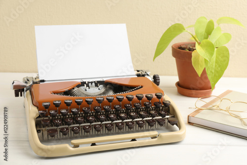 Vintage typewriter with sheet of paper, glasses, notebook and houseplant on white wooden table
