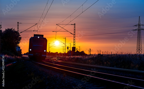 Modern electric railcar in a curve of the double-track main line from Paderborn to Altenbeken (Germany). Railroad panorama with colorful sunset and low sun behind the fast train. Idyllic atmosphere. photo