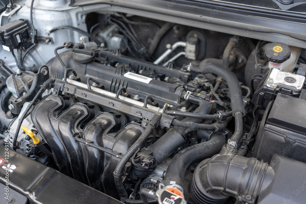 A car engine bay with various components including the intake manifold, hoses, wiring, and fluid reservoirs. The engine appears to be a modern internal combustion engine. A car engine bay with various components including the intake manifold, hoses, wiring, and fluid reservoirs. The engine appears to be a modern internal combustion engine.