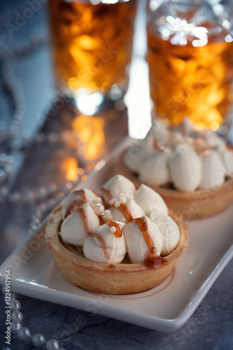 Two tarts topped with whipped cream and caramel drizzle on a white plate, with two glasses of iced tea in the background.