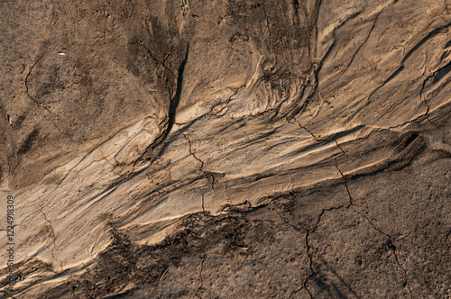Cracked, dry earth with layered sedimentary rock formations, displaying erosion patterns and geological textures