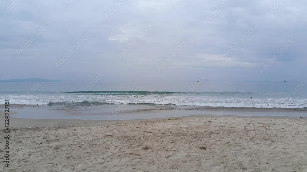 Overcast sky above gentle ocean waves rolling onto a sandy beach, creating a serene coastal scene Overcast sky above gentle ocean waves rolling onto a sandy beach, creating a serene coastal scene