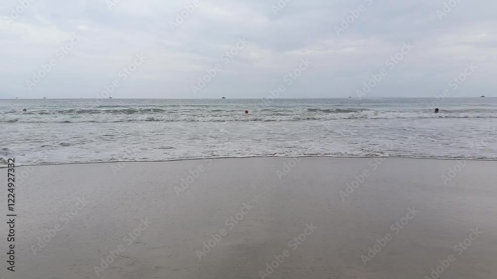 Calm ocean waves gently lapping against a sandy beach under a cloudy sky Calm ocean waves gently lapping against a sandy beach under a cloudy sky