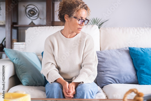 A woman sitting alone on the couch at home, looking down with a sad expression, feeling emotionally drained and reflecting on relationship issues and personal struggles during menopause, burnout