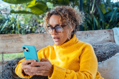 Photos A mature woman with blonde curly hair wearing glasses and a yellow sweater sitti