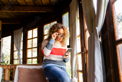 Woman using her smartphone at home to browse the internet, send messages, chat with friends, and manage remote work tasks while relaxing in the comfort of her living space and enjoying leisure time photo