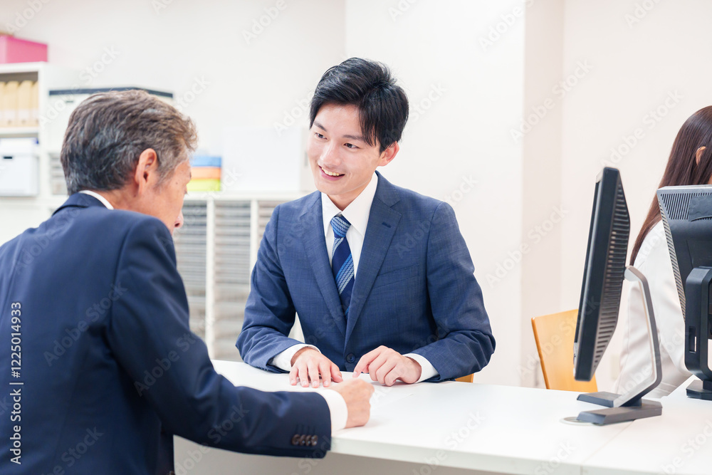 窓口で高齢者の来客の対応をする男性 窓口で高齢者の来客の対応をする男性