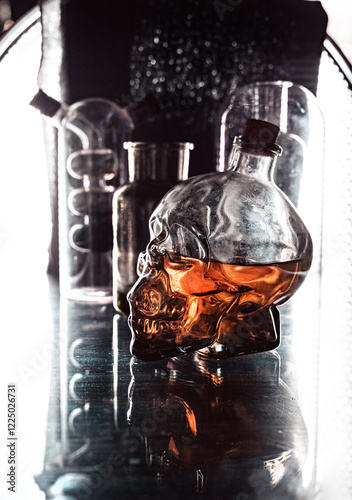 Glass skull whiskey bottle and mystical flasks on a black background with a beautiful background light