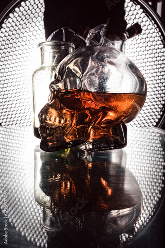 Obraz na płótnie Glass skull whiskey bottle and mystical flasks on a black background with a beautiful background light w salonie