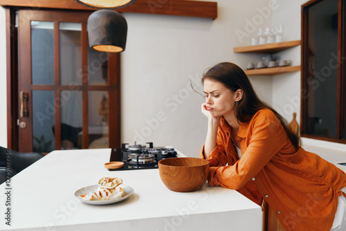 Quadro em tela A thoughtful woman in an orange outfit contemplating over a bowl in a modern kit